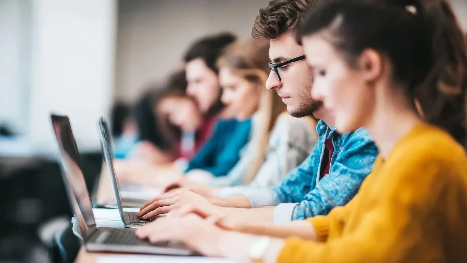 Adult learners seated in a row concentrate on their laptops during a training session
